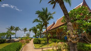 Un complexe hôtelier tropical avec des palmiers, un sentier et un bâtiment doté d’un toit en tuiles.