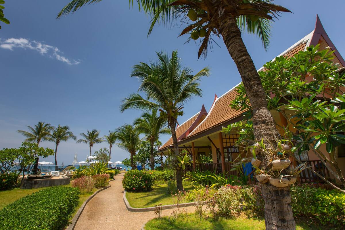 Un complexe hôtelier tropical avec des palmiers, un sentier et un bâtiment doté d’un toit en tuiles.