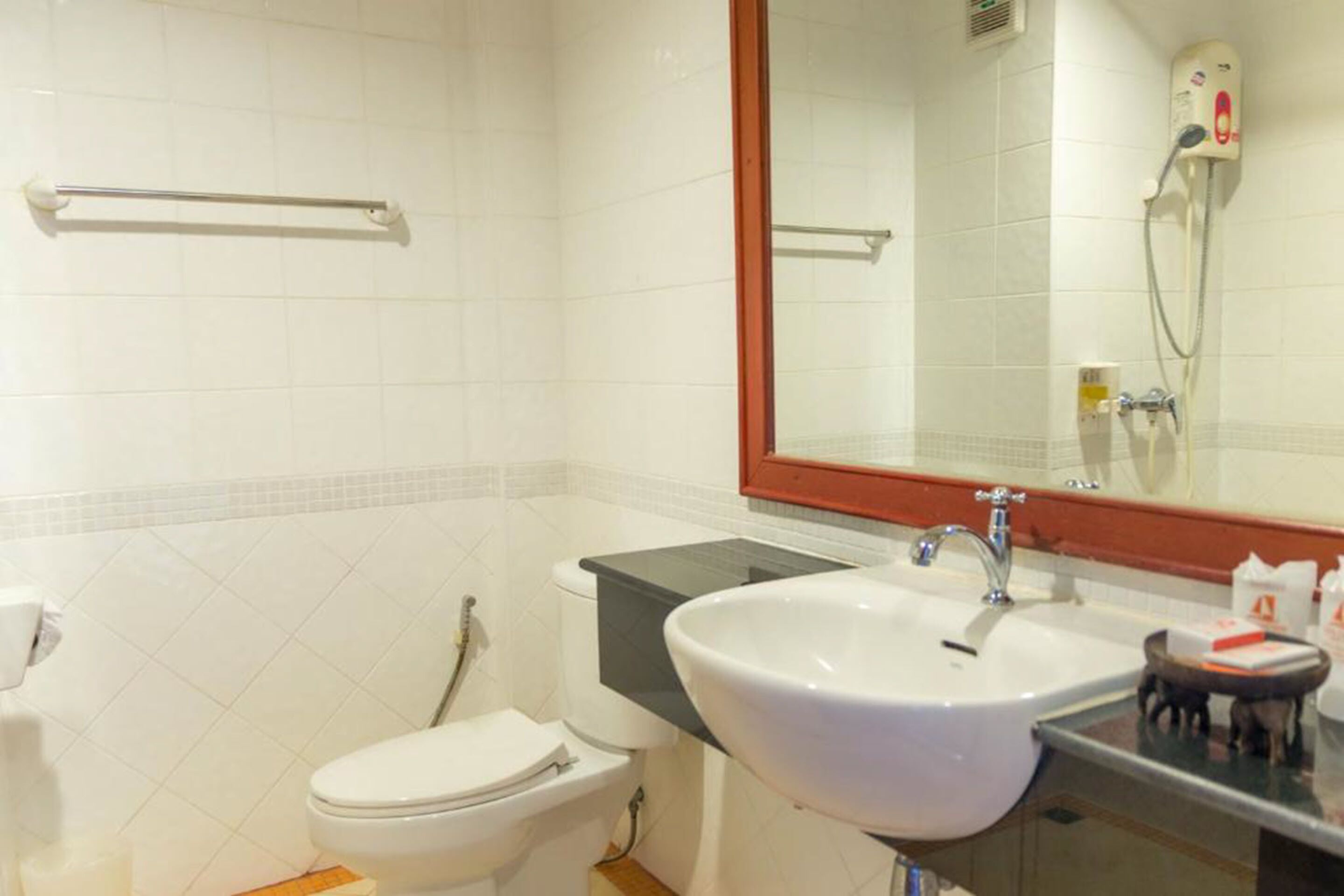 Un baño con inodoro blanco, lavabo con espejo y cabezal de ducha en la pared.