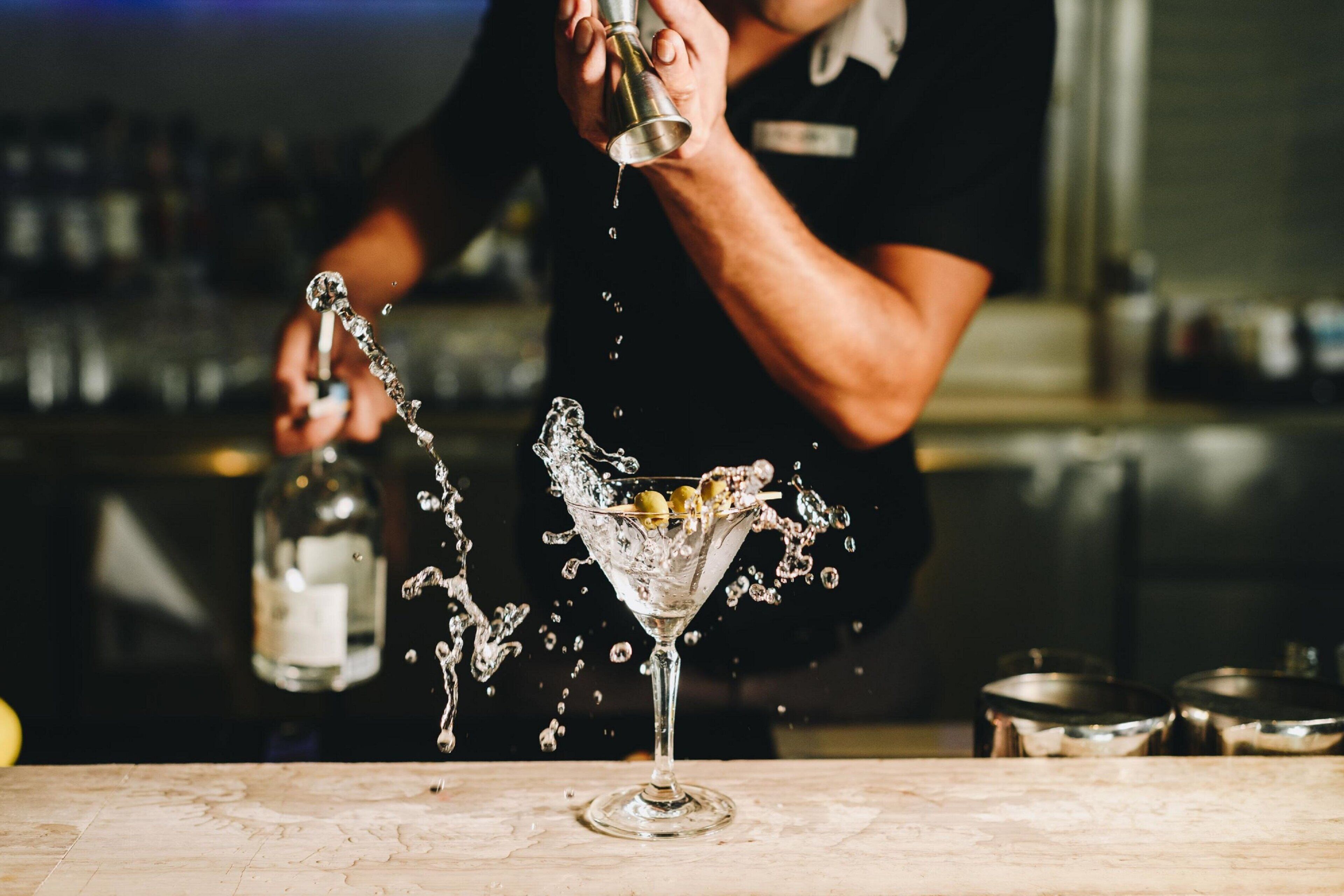 A bartender pouring a drink into a martini glass, with water splashing out.
