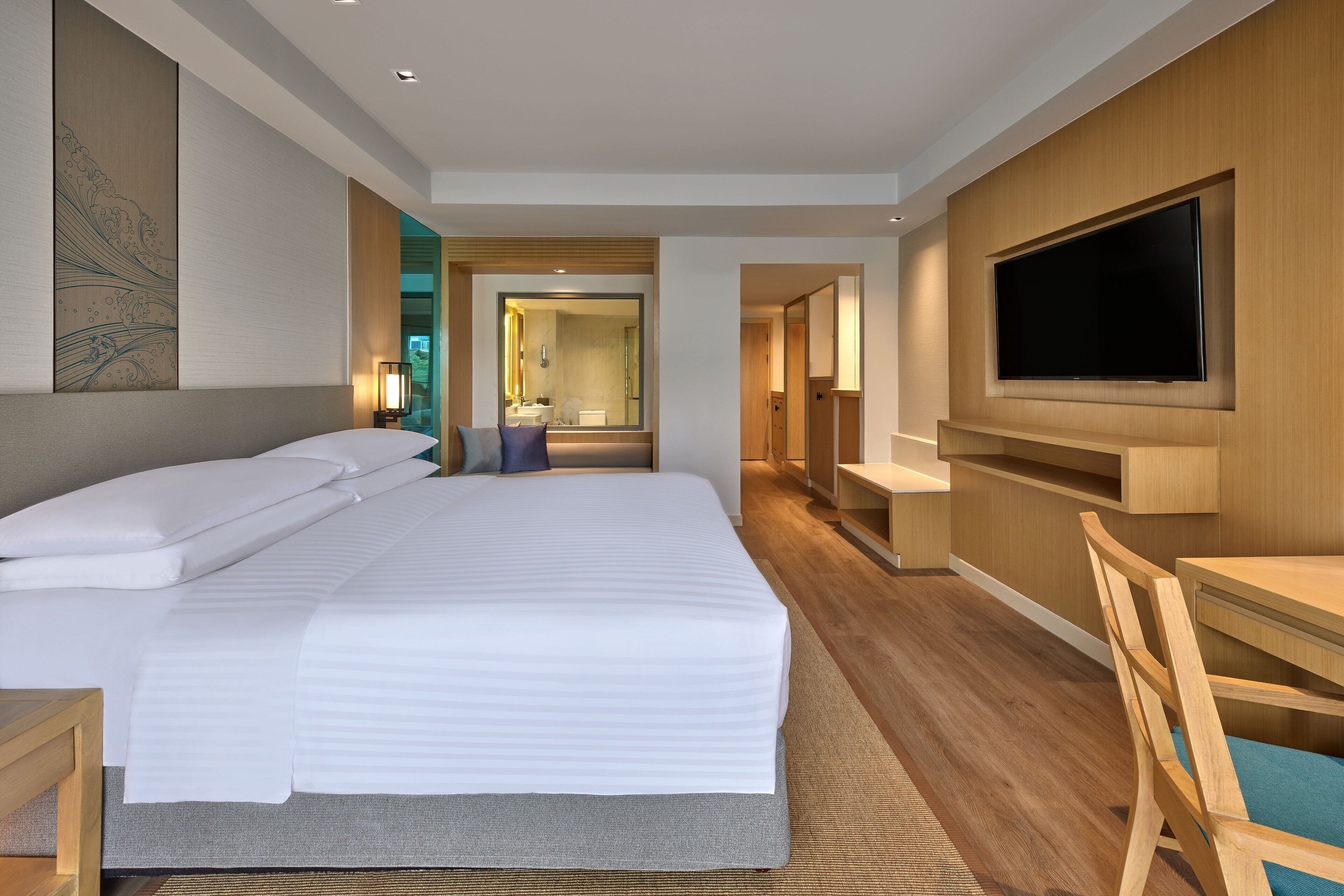 Une chambre d’hôtel moderne avec un grand lit, un téléviseur fixé au mur et un bureau avec une chaise.