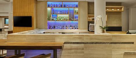 A bar area with a wooden counter, marble flooring, and a variety of liquor bottles.