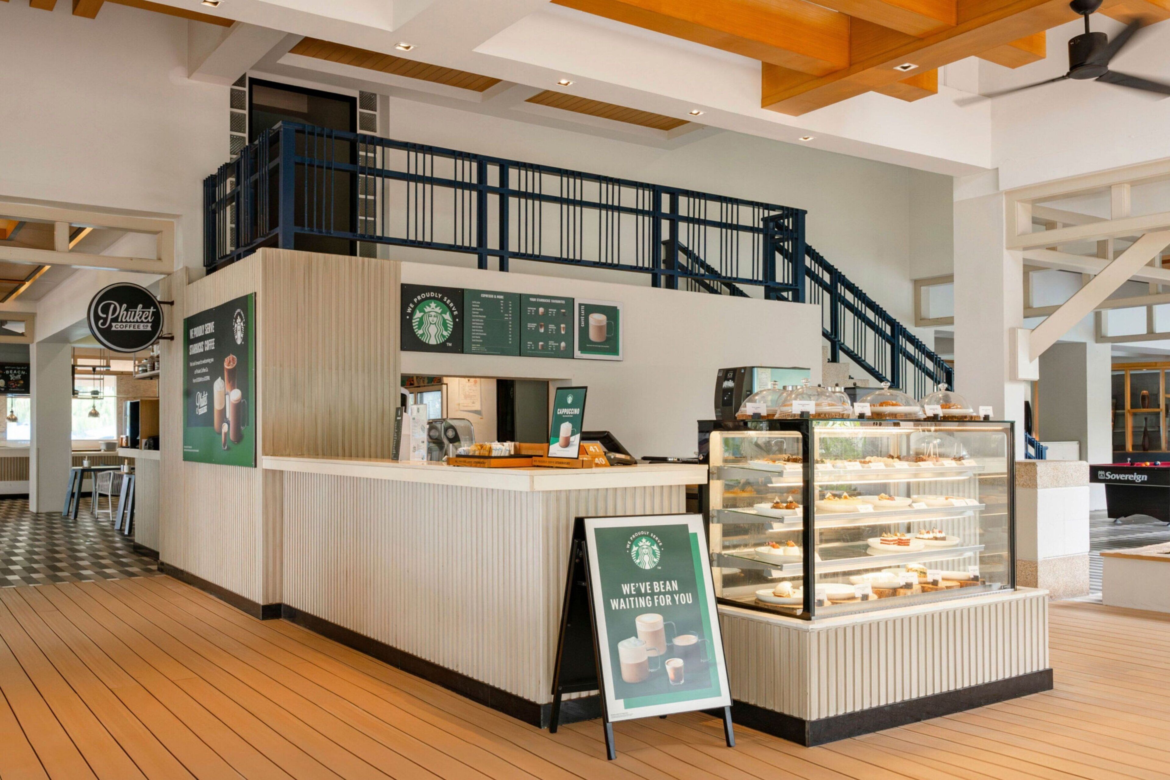 A Starbucks coffee shop with a counter, a display case with pastries, and a staircase leading to a second floor.