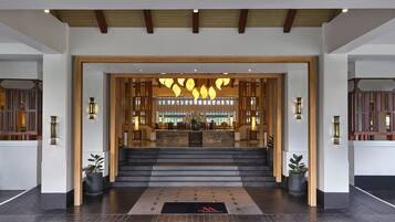Un hall d’hôtel comprenant un comptoir d’accueil, un escalier menant à l’étage supérieur et un luminaire décoratif placé au-dessus de l’entrée.