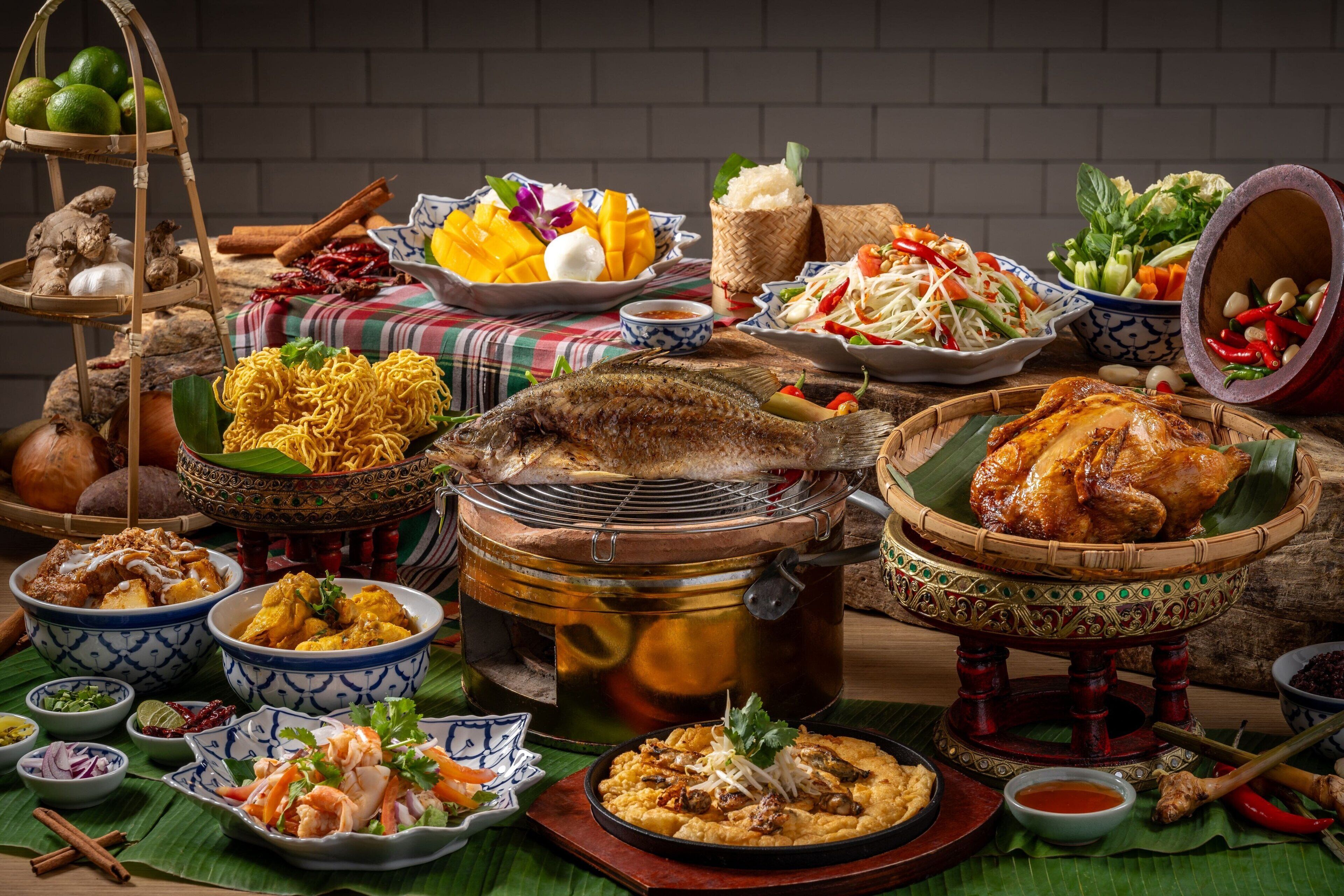 Variedad de platos y alimentos sobre una mesa, incluyendo un pescado entero, un bol de fideos y varios acompañamientos.