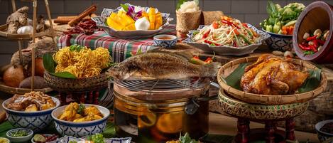 Variedad de platos y alimentos sobre una mesa, incluyendo un pescado entero, un bol de fideos y varios acompañamientos.