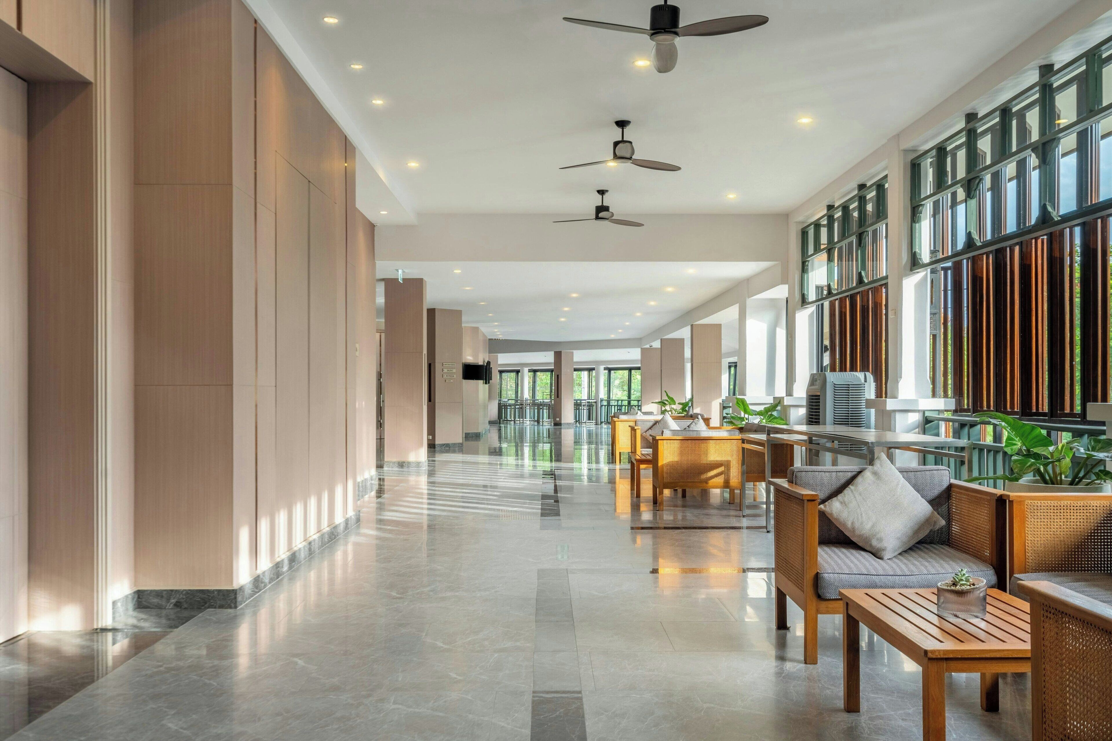 A spacious lobby with high ceilings, ceiling fans, and a long corridor leading to a seating area with tables and chairs.