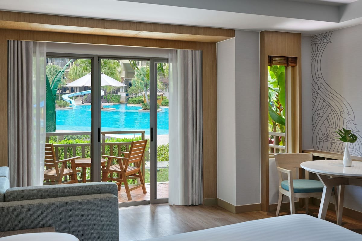 A hotel room with a large sliding glass door leading to a pool area, a dining table, and a bed.