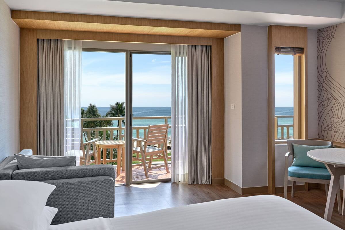 A hotel room with a balcony, a bed, a sofa, a table, and a chair.
