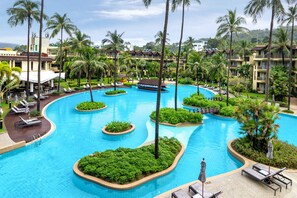A resort with a large central pool surrounded by palm trees and lounge areas.