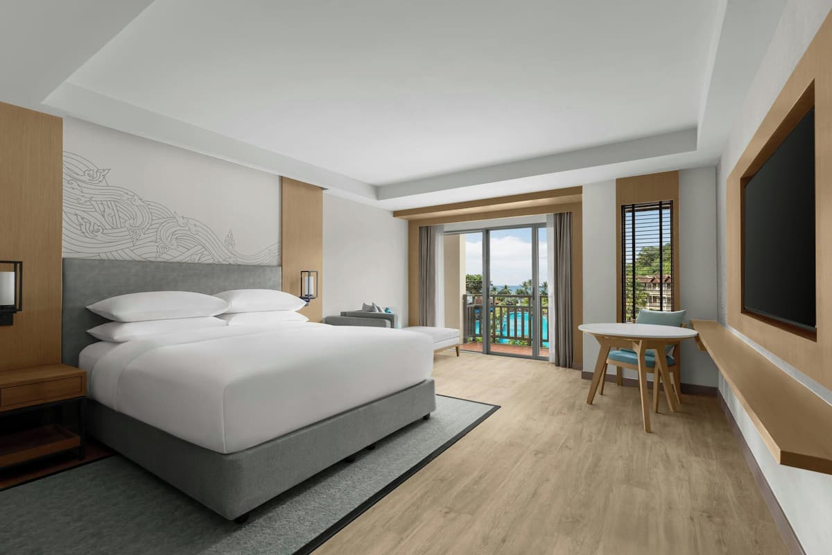 A modern hotel room with a large bed, a desk, and a view of a swimming pool.