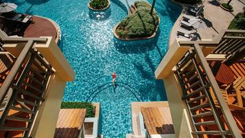 A large swimming pool with a central island, surrounded by lounge chairs and umbrellas.