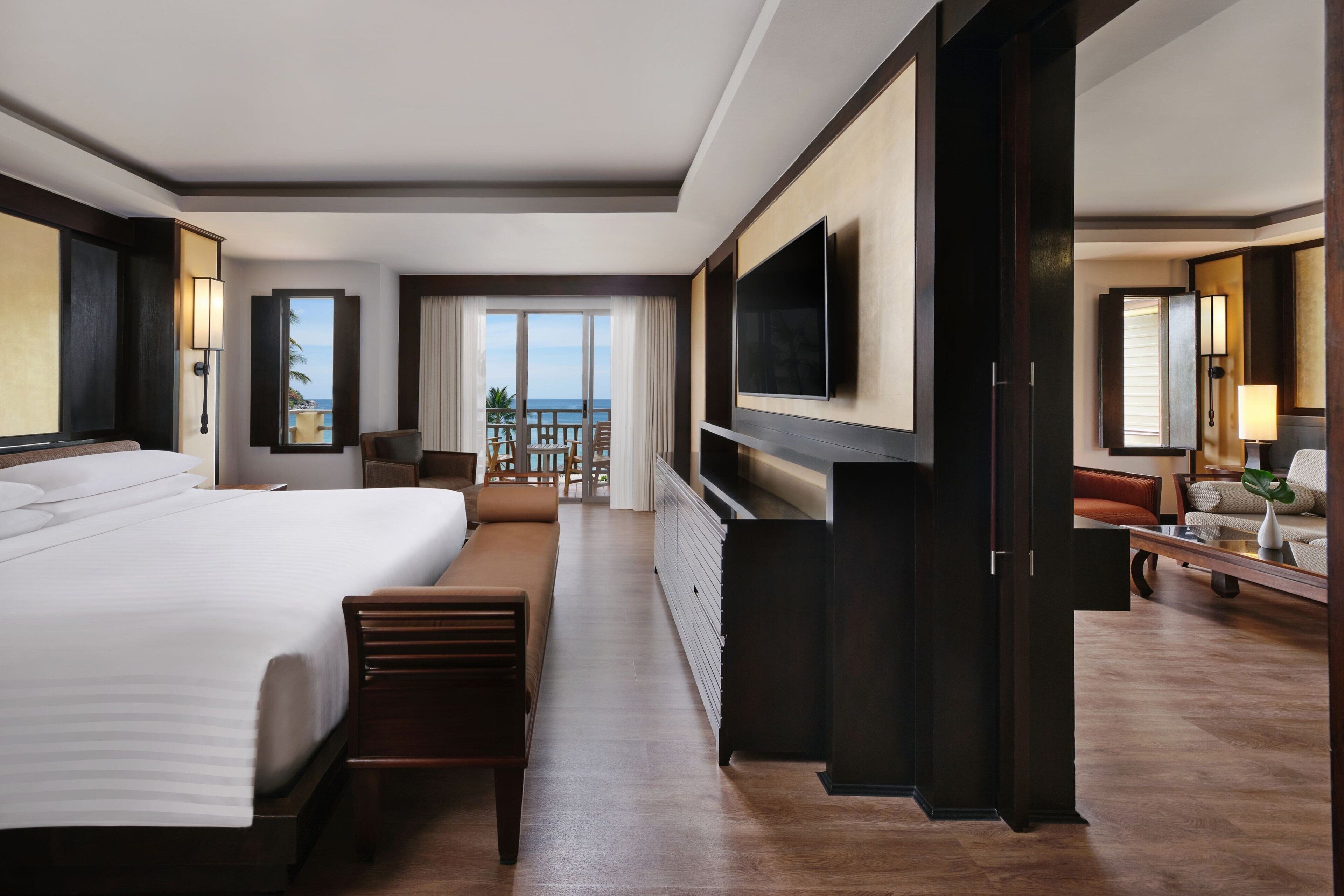 Une chambre d’hôtel dotée d’un grand lit, d’un téléviseur fixé au mur, d’un balcon avec vue sur la mer et d’un coin salon avec une table et des chaises.