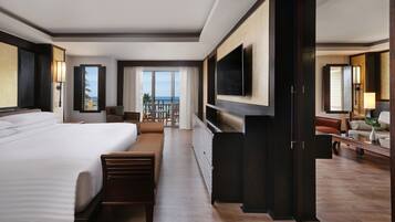 Ein Hotelzimmer mit einem großen Bett, einem an der Wand montierten Fernseher, einem Balkon mit Meerblick und einer Sitzecke mit Tisch und Stühlen.