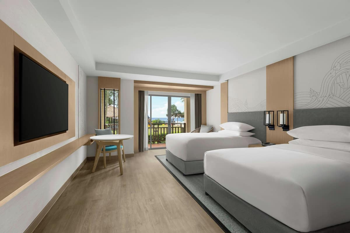 A hotel room with two beds, a TV, a small table, and a balcony with a view.