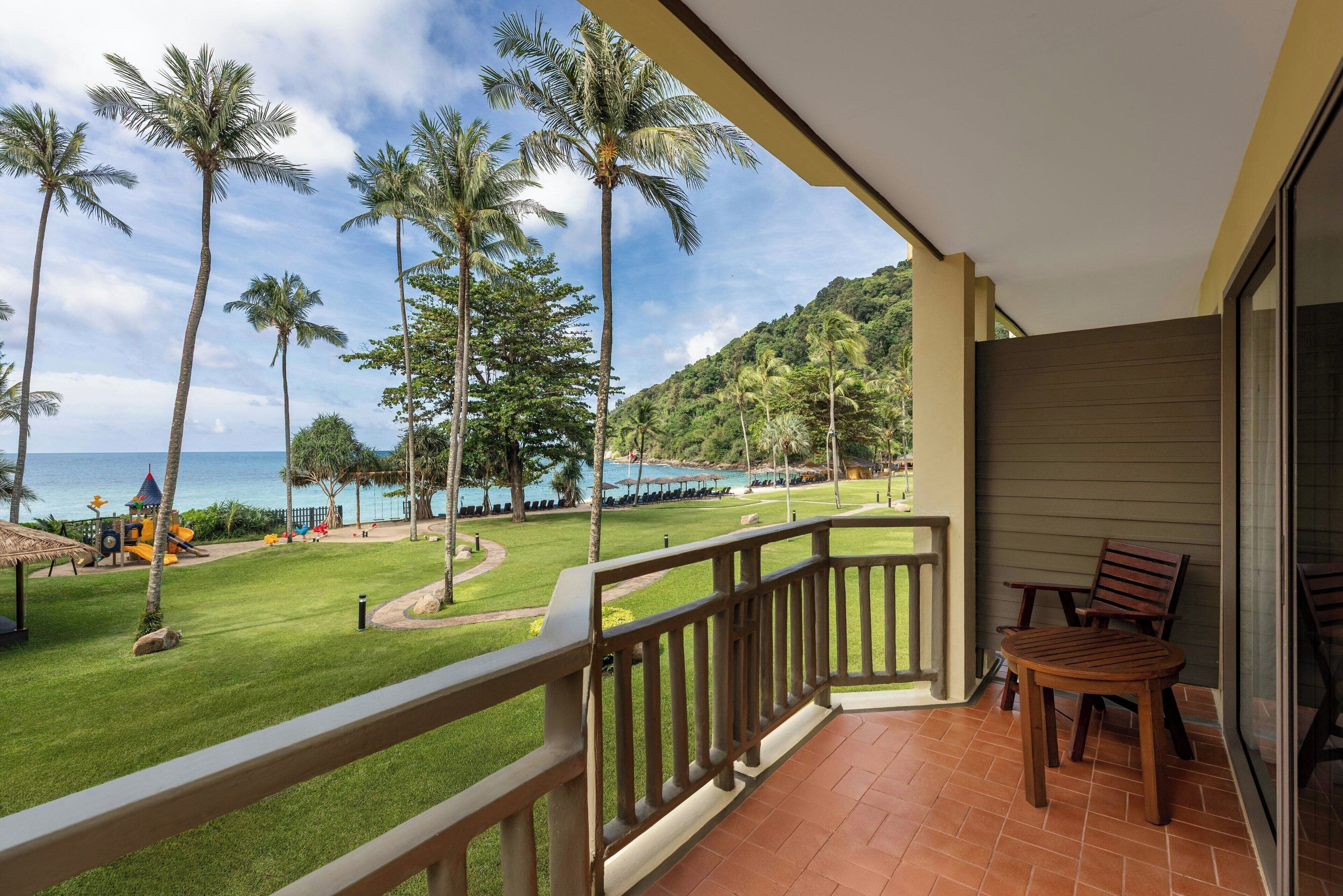 A balcony with a view of a beach, palm trees, and a golf course.