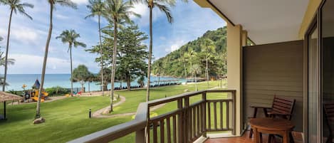 A balcony with a view of a beach, palm trees, and a golf course.