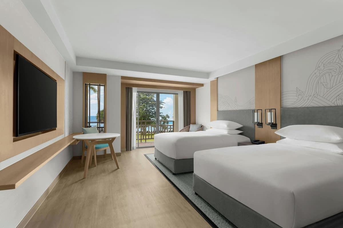 A hotel room with two beds, a desk, a TV, and a balcony with a view.