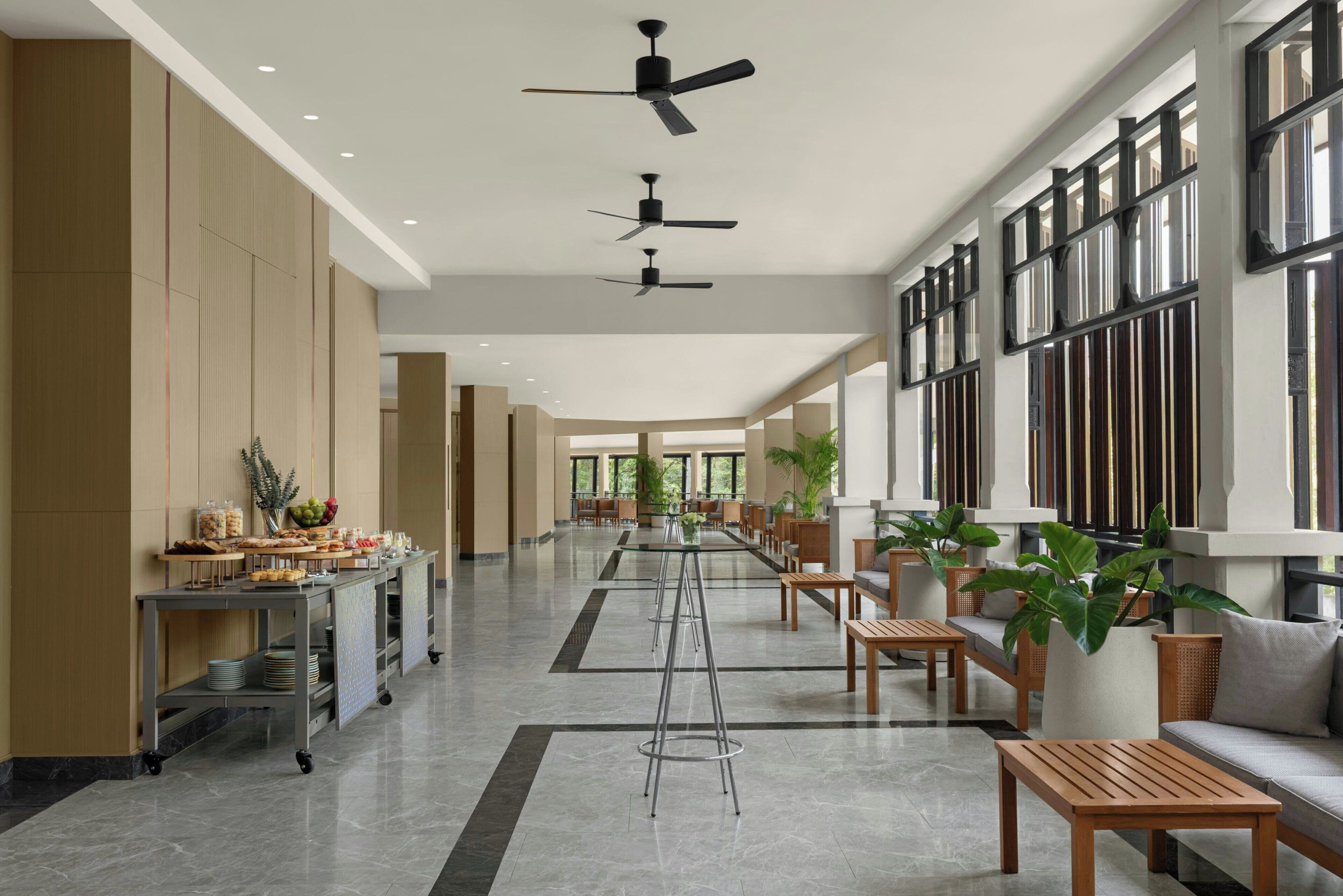 A spacious lobby with a long reception desk, seating area, and ceiling fans.