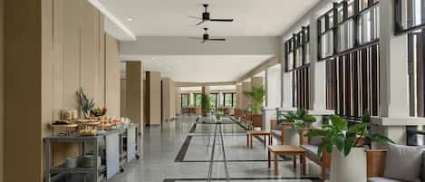 A spacious lobby with a long reception desk, seating area, and ceiling fans.