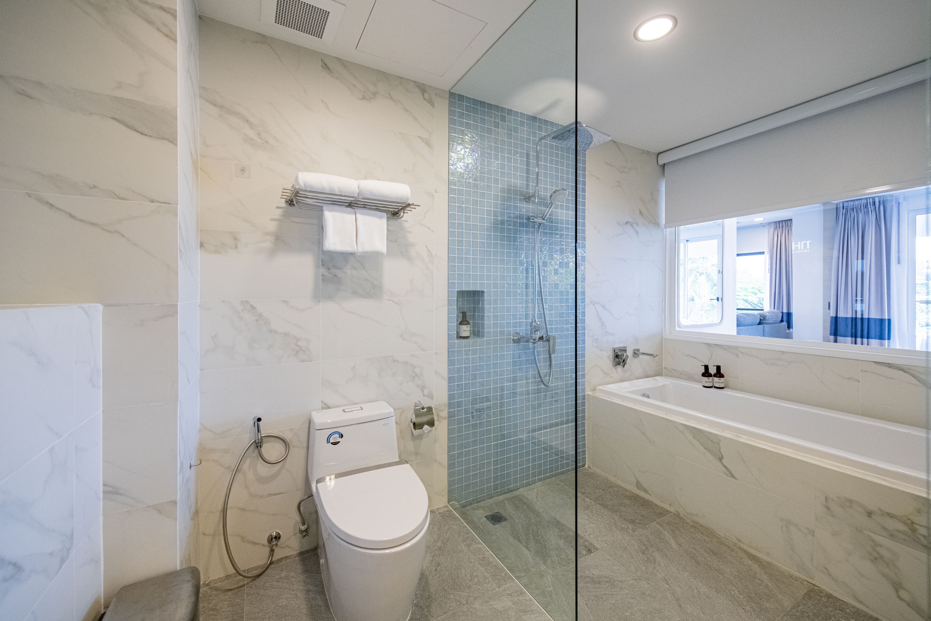 A modern bathroom with a marble floor, a glass-enclosed shower, a white toilet, and a large bathtub.