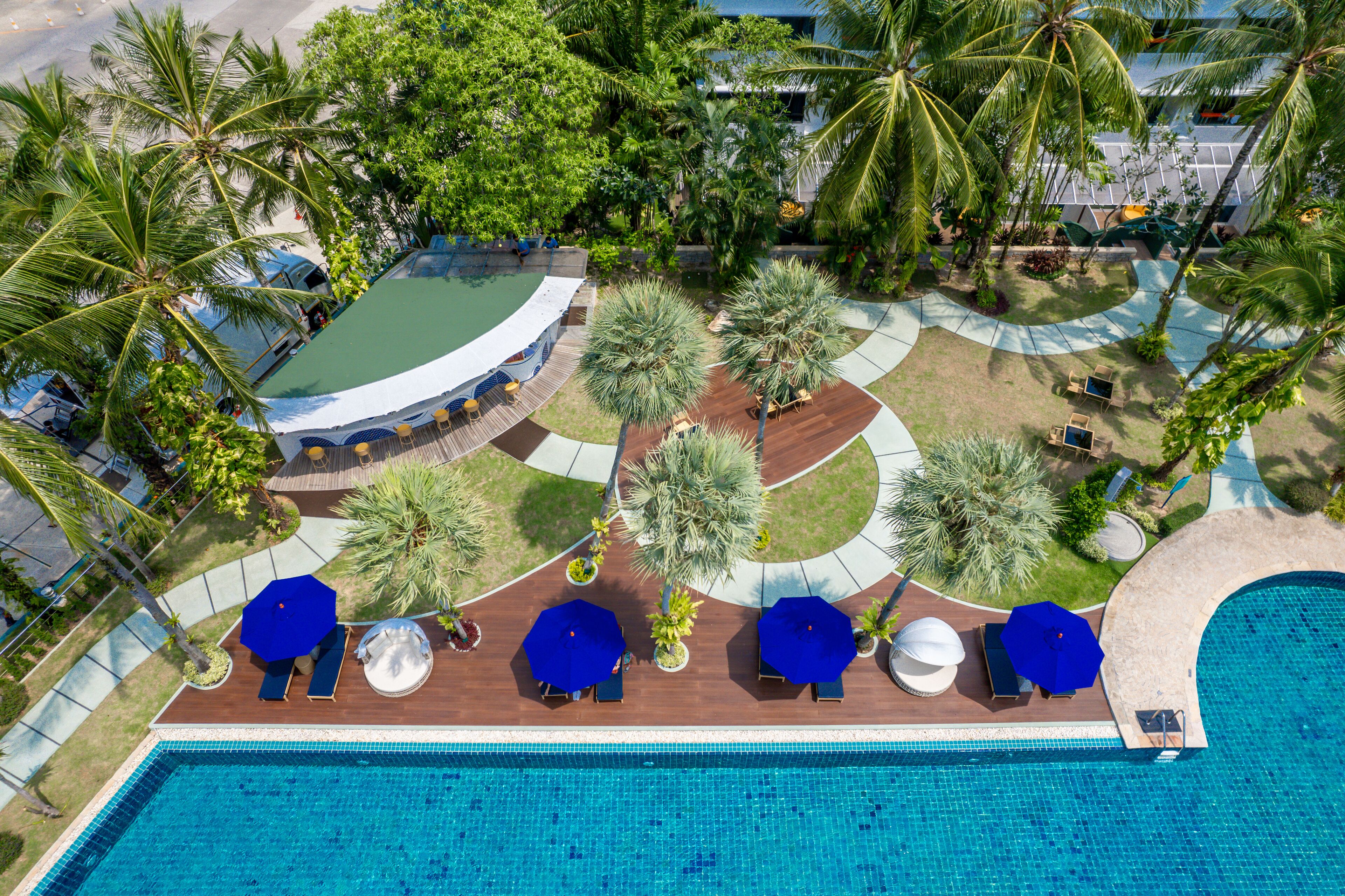 An aerial view of a resort with a swimming pool, lounge chairs, and palm trees.