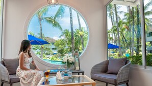 A room with a large round window, a round table, two wicker chairs, and a sofa. - NH Boat Lagoon Phuket Resort (Ko Kaeo)