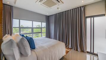 A modern bedroom with a large bed, grey curtains, and a view of greenery outside.