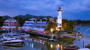 A marina with boats docked, a prominent lighthouse, and buildings with outdoor seating areas. - NH Boat Lagoon Phuket Resort (Ko Kaeo)