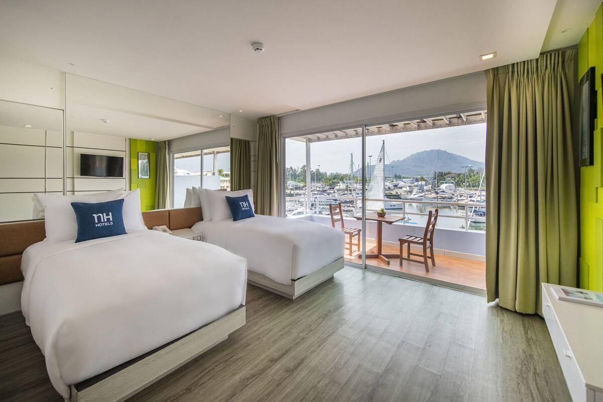 Quarto de hotel com duas camas, varanda com vista para barcos e montanhas, e televisão na parede.
