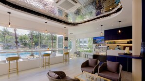 A modern lounge area with wicker furniture, a glass coffee table, and a view of a pool and greenery outside. - NH Boat Lagoon Phuket Resort (Ko Kaeo)
