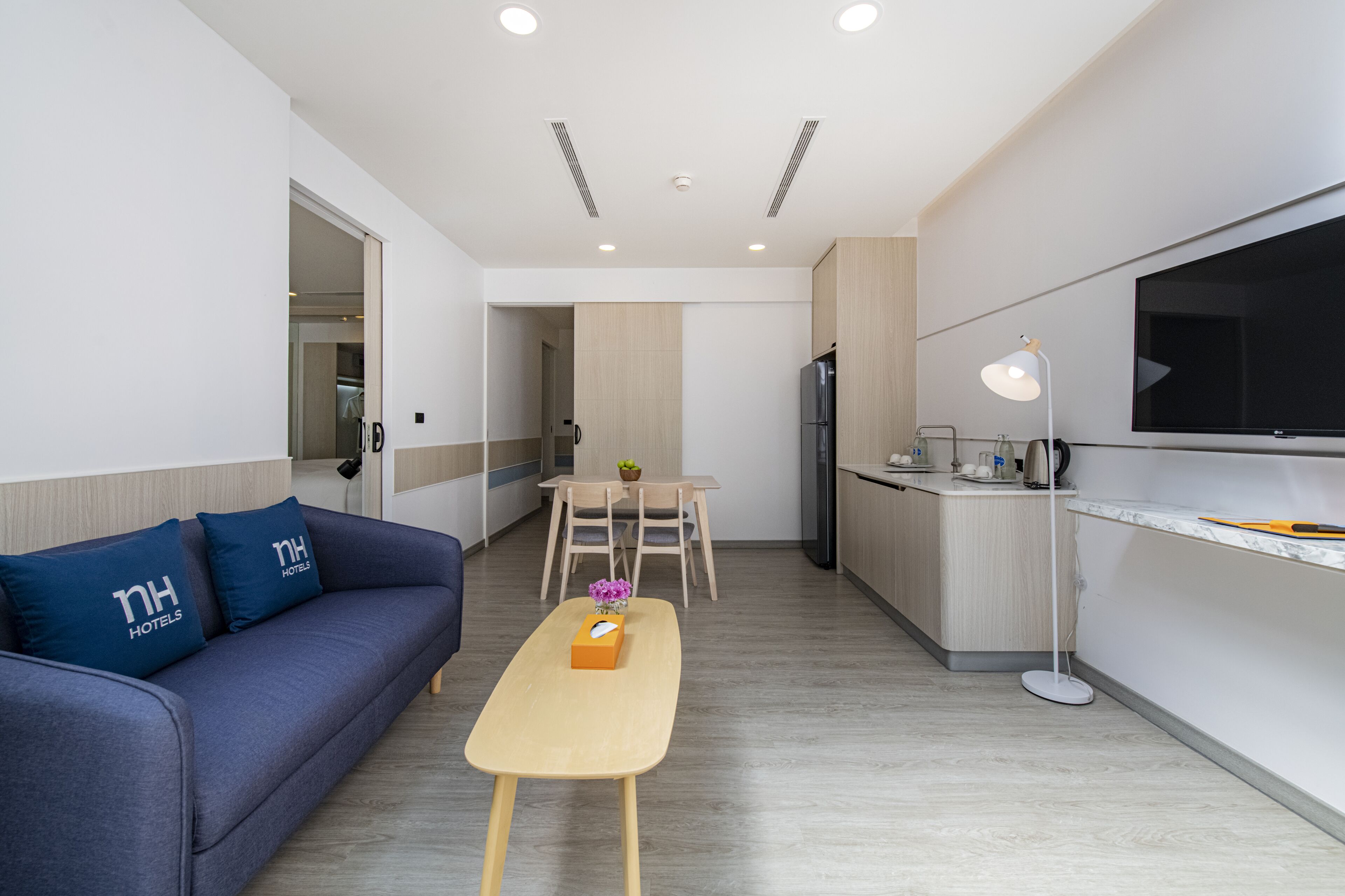 Una habitación de hotel moderna con sofá, una pequeña mesa, televisión, zona de cocina y mesa de comedor.
