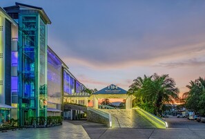 Una entrada de hotel moderna con fachada de vidrio, un cartel llamativo del Resort Boat Lagoon Phuket y una escalera que conduce a la entrada.