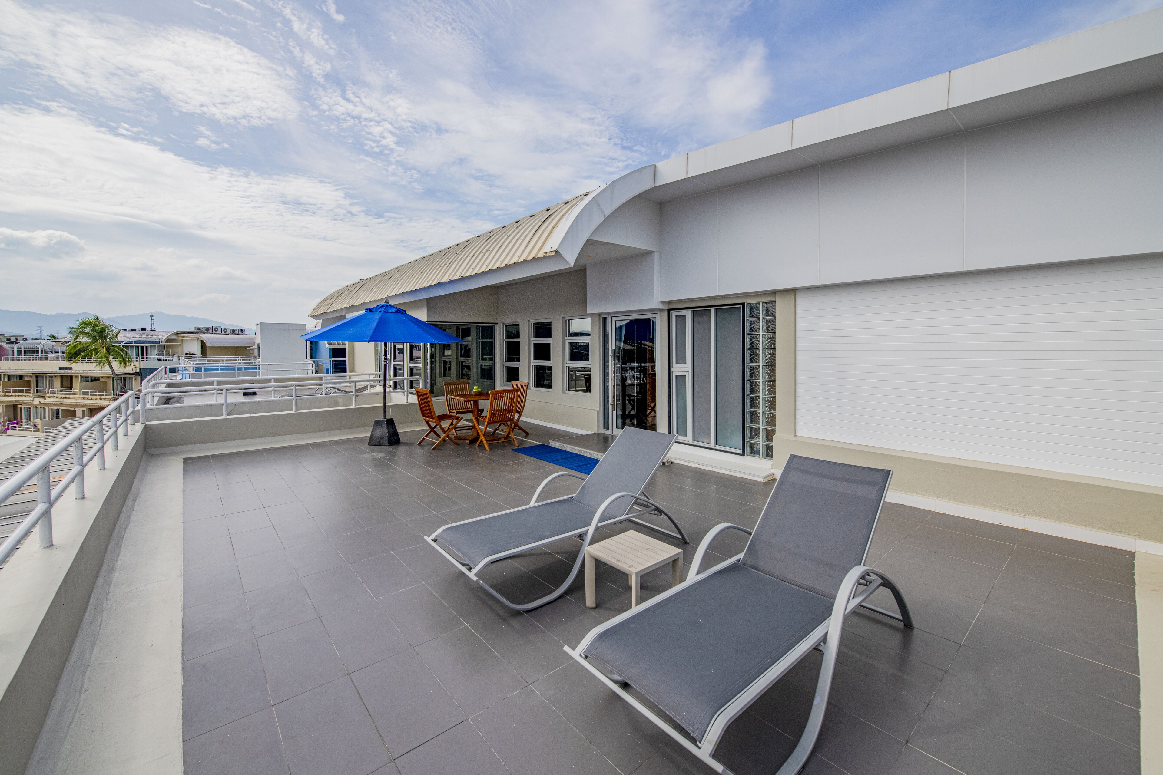 A rooftop terrace with two lounge chairs, a table, and a blue umbrella.