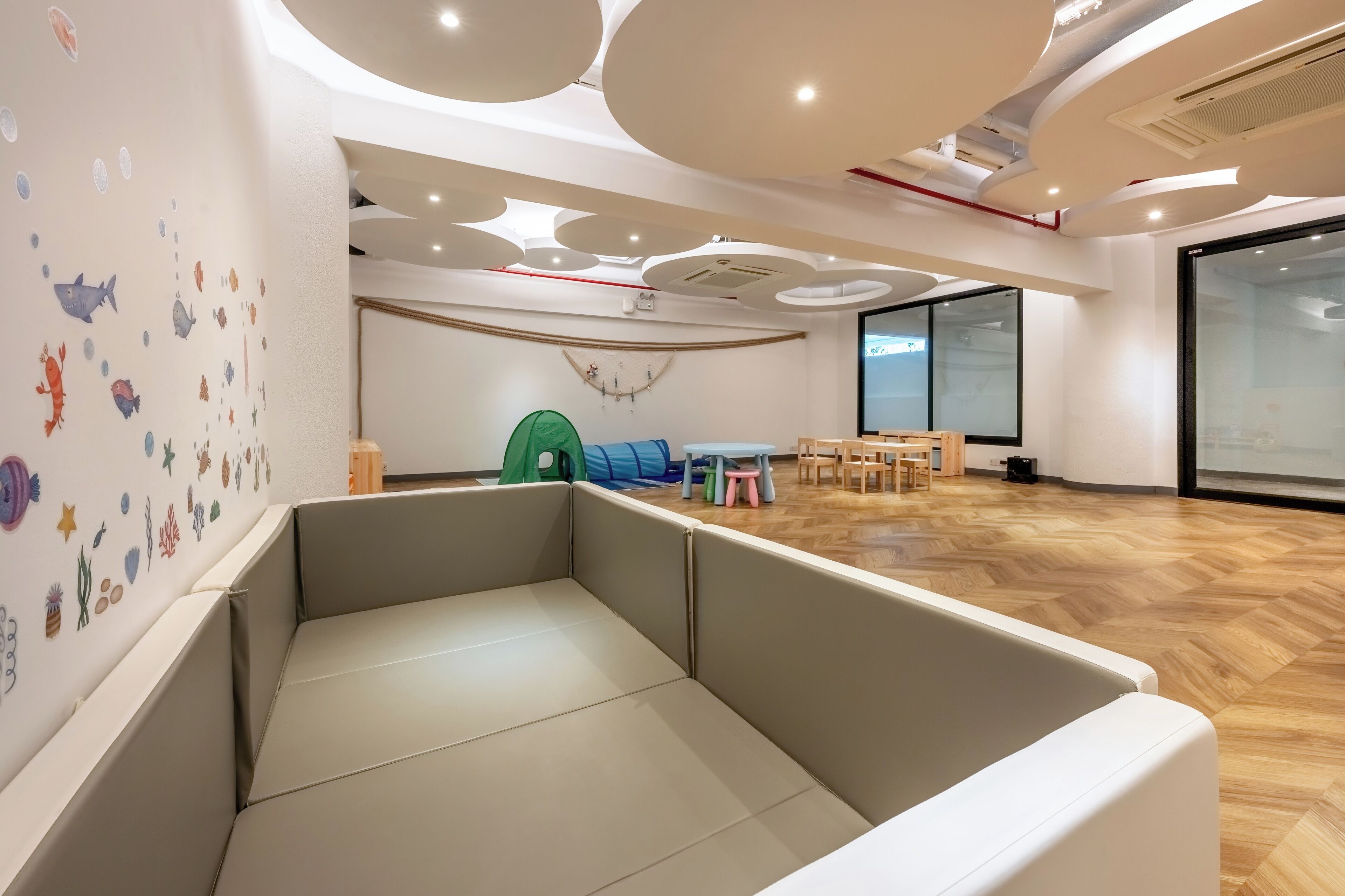 A modern room with a wooden floor, a cushioned seating area, a small table, and a green play tent.