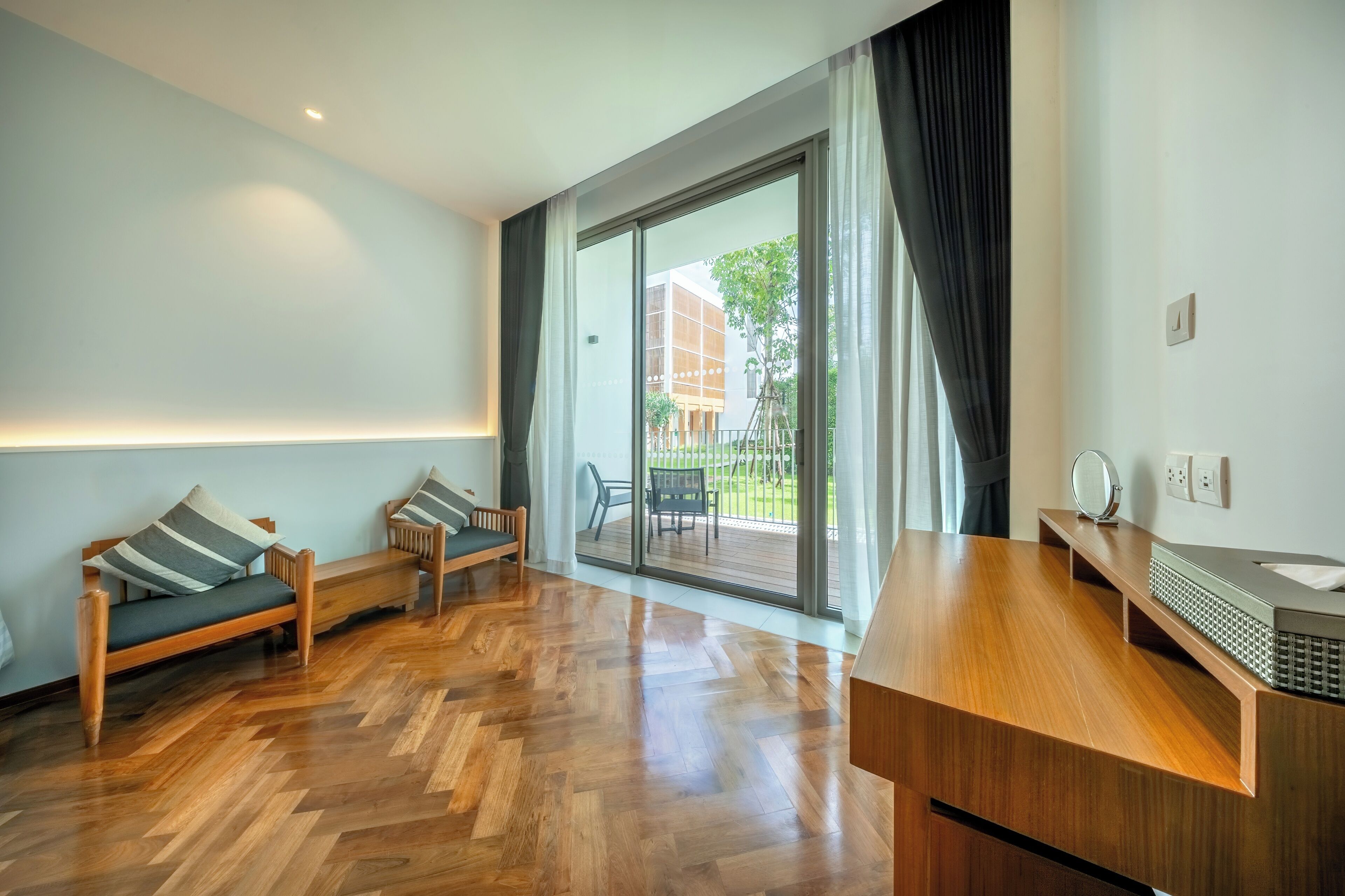 Une pièce moderne avec un plancher en bois, deux canapés, une grande porte-fenêtre coulissante donnant sur un espace extérieur, et un comptoir en bois agrémenté d’un miroir et d’un évier.