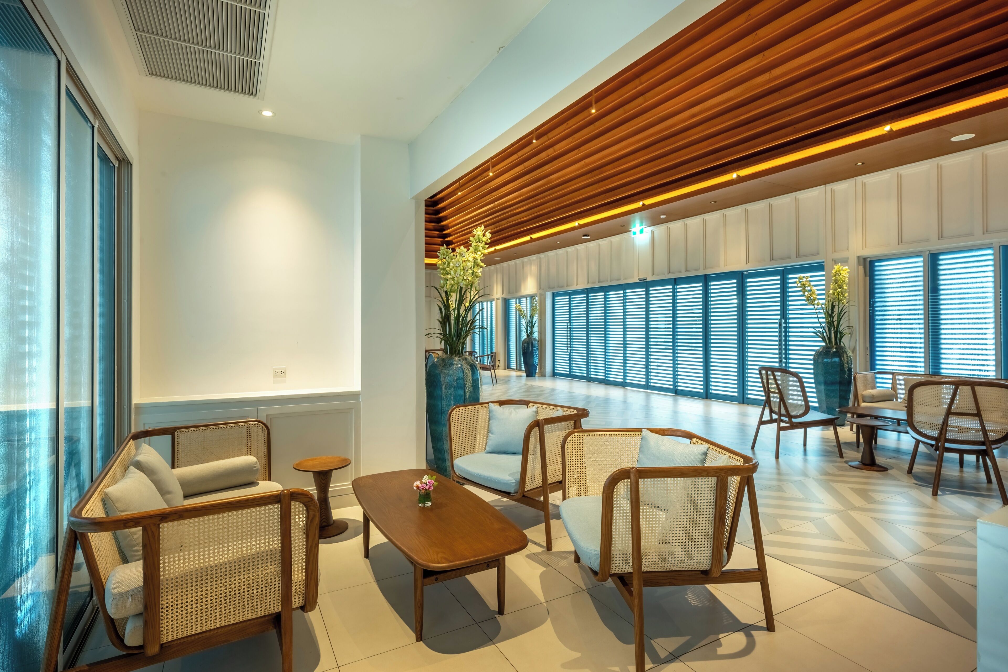 A spacious lobby with wicker furniture, a wooden ceiling, and large windows.