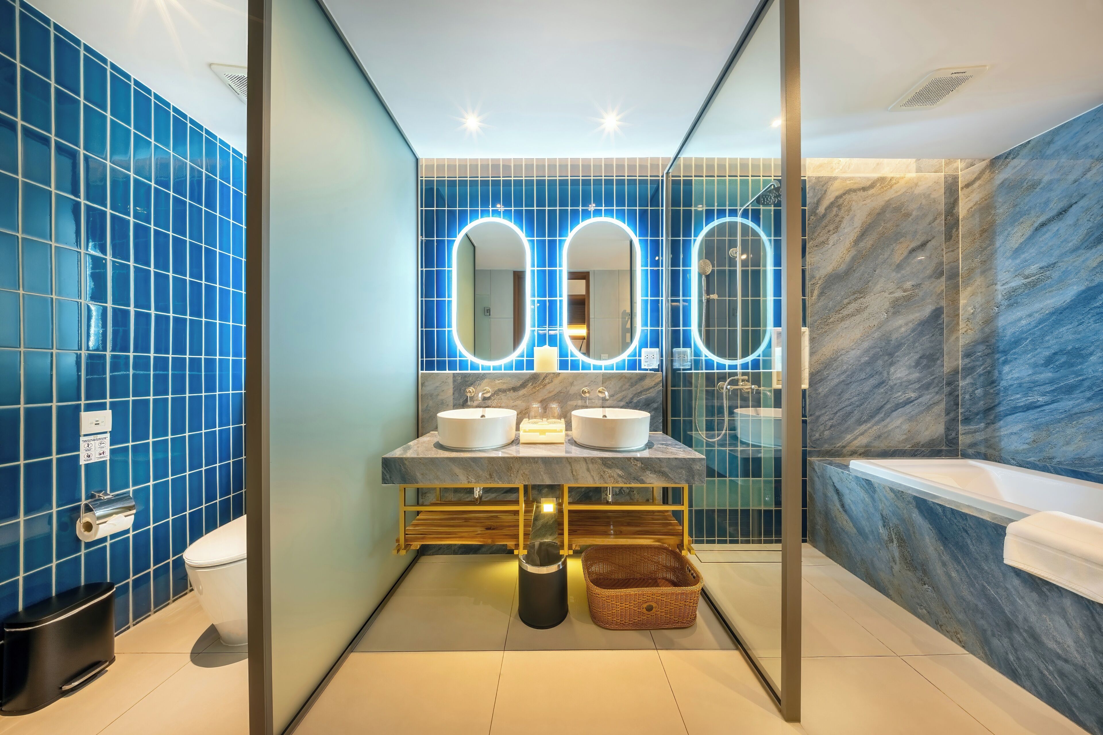A modern bathroom with blue tiled walls, two sinks, a mirror, and a bathtub.