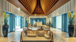 A modern lobby with a central reception desk, seating area, and large windows with blue shutters. - Patong Beach Hotel by See2Sea (Patong)