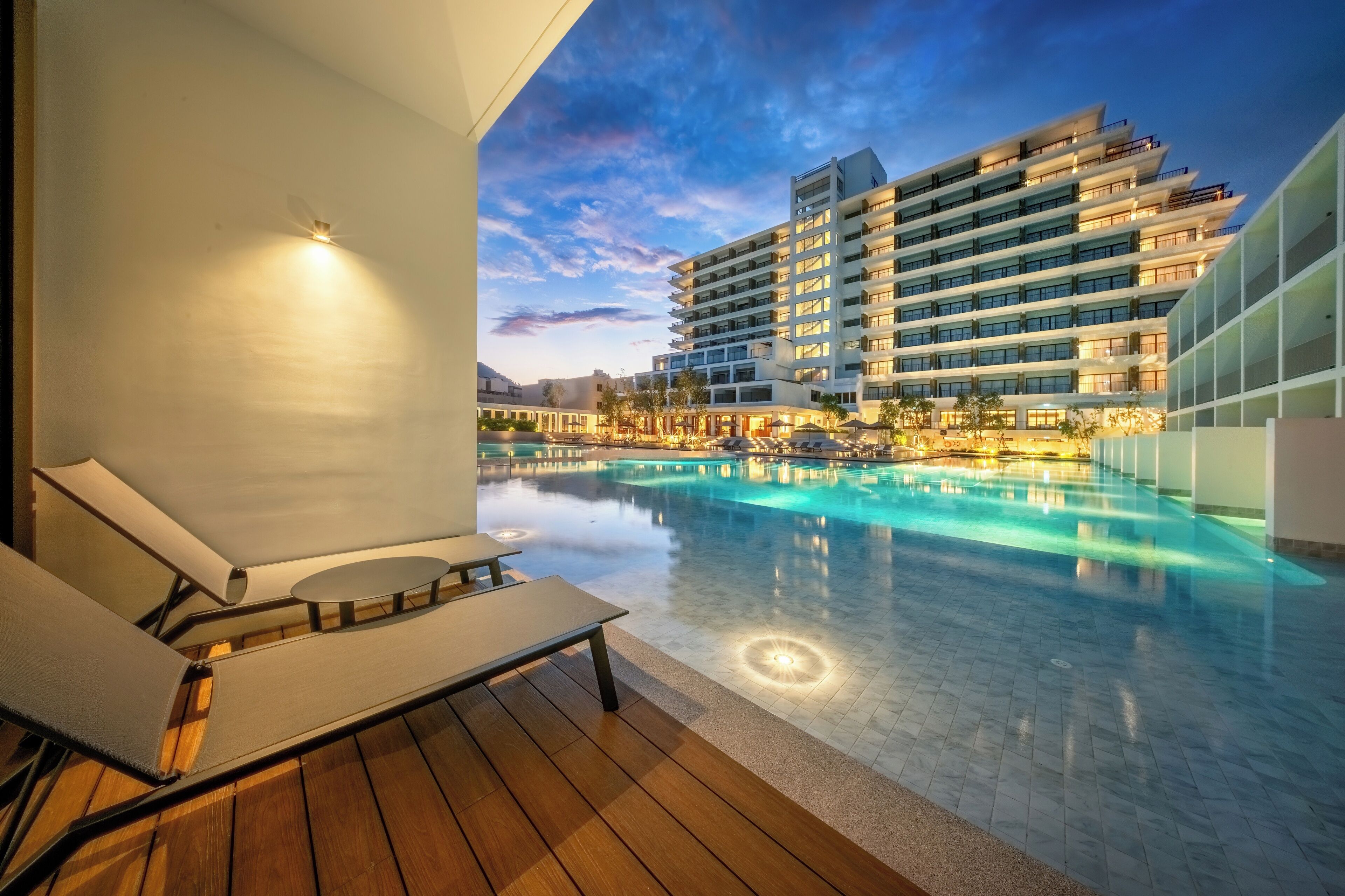 Un hotel moderno con piscina, sillones de descanso y vistas al edificio.