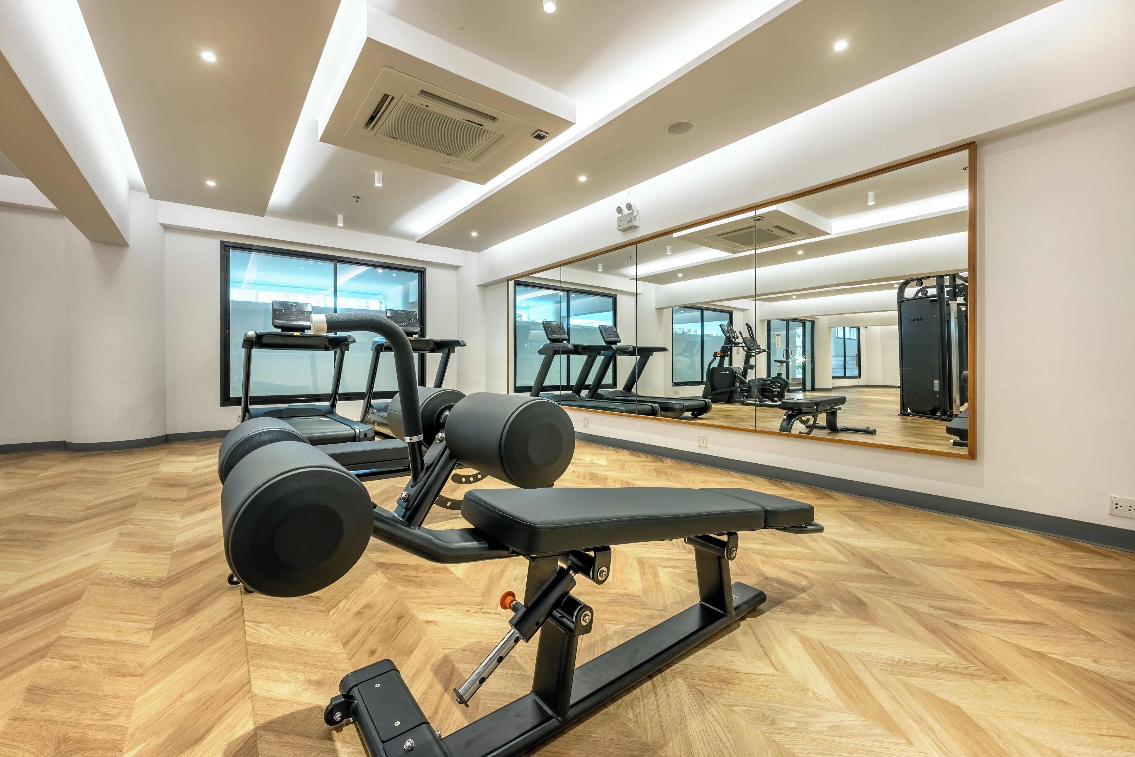 A gym with exercise equipment, large windows, and a mirrored wall.