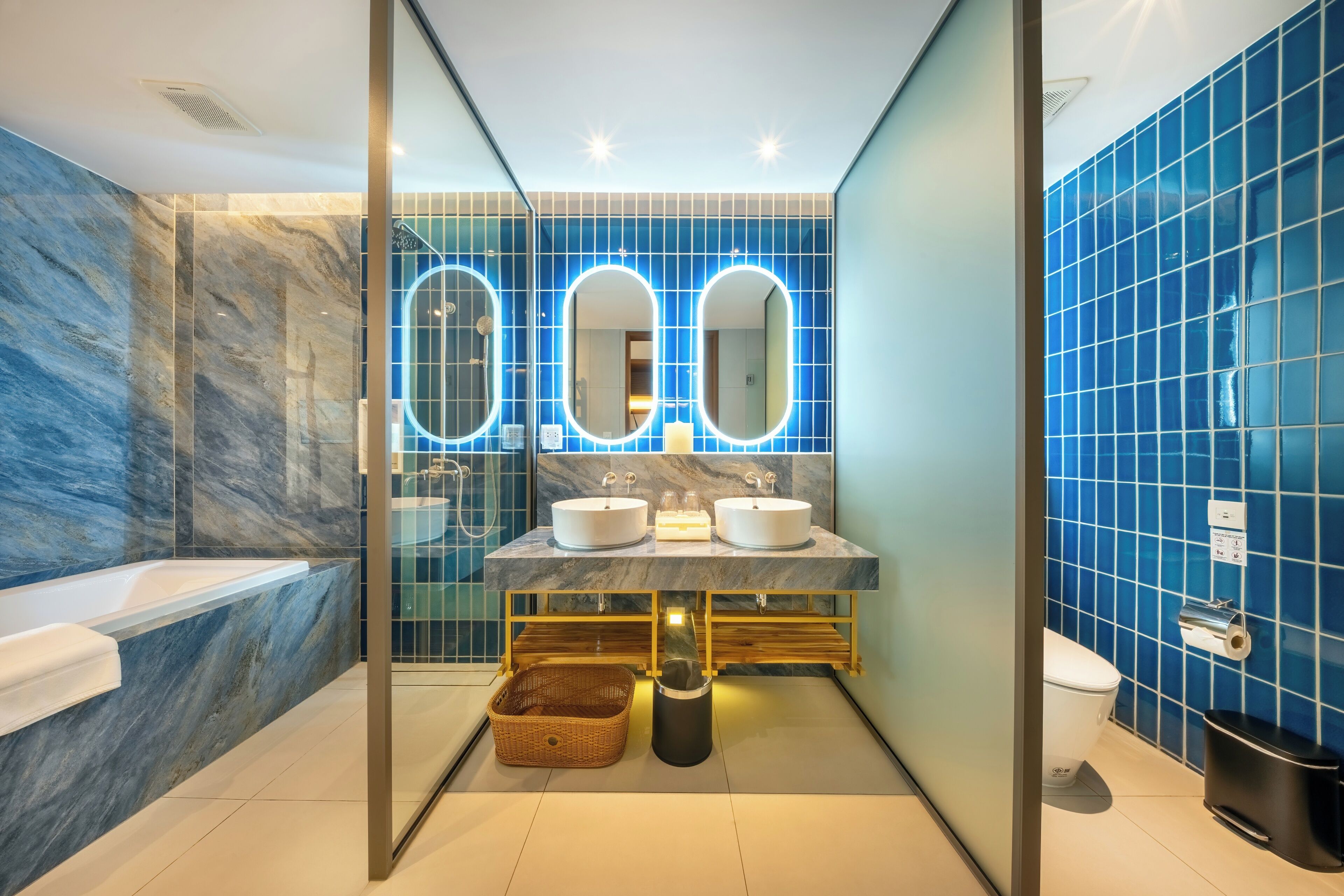 Un baño moderno con paredes de mármol, una bañera, dos lavamanos y un inodoro.