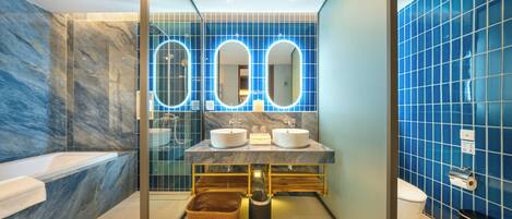Un baño moderno con paredes de mármol, una bañera, dos lavamanos y un inodoro.