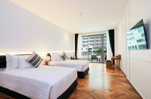 A hotel room with two beds, a TV, a balcony with a view of buildings, and a wooden floor. - Patong Beach Hotel by See2Sea (Patong)