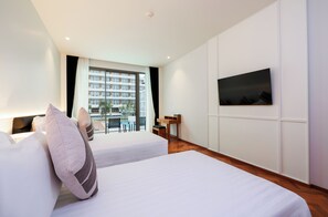 A hotel room with two beds, a TV, a desk, and a view of a building outside. - Patong Beach Hotel by See2Sea (Patong)