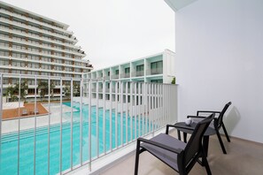 A balcony with a pool view, a dining table with chairs, and a white building in the background. - Patong Beach Hotel by See2Sea (Patong)