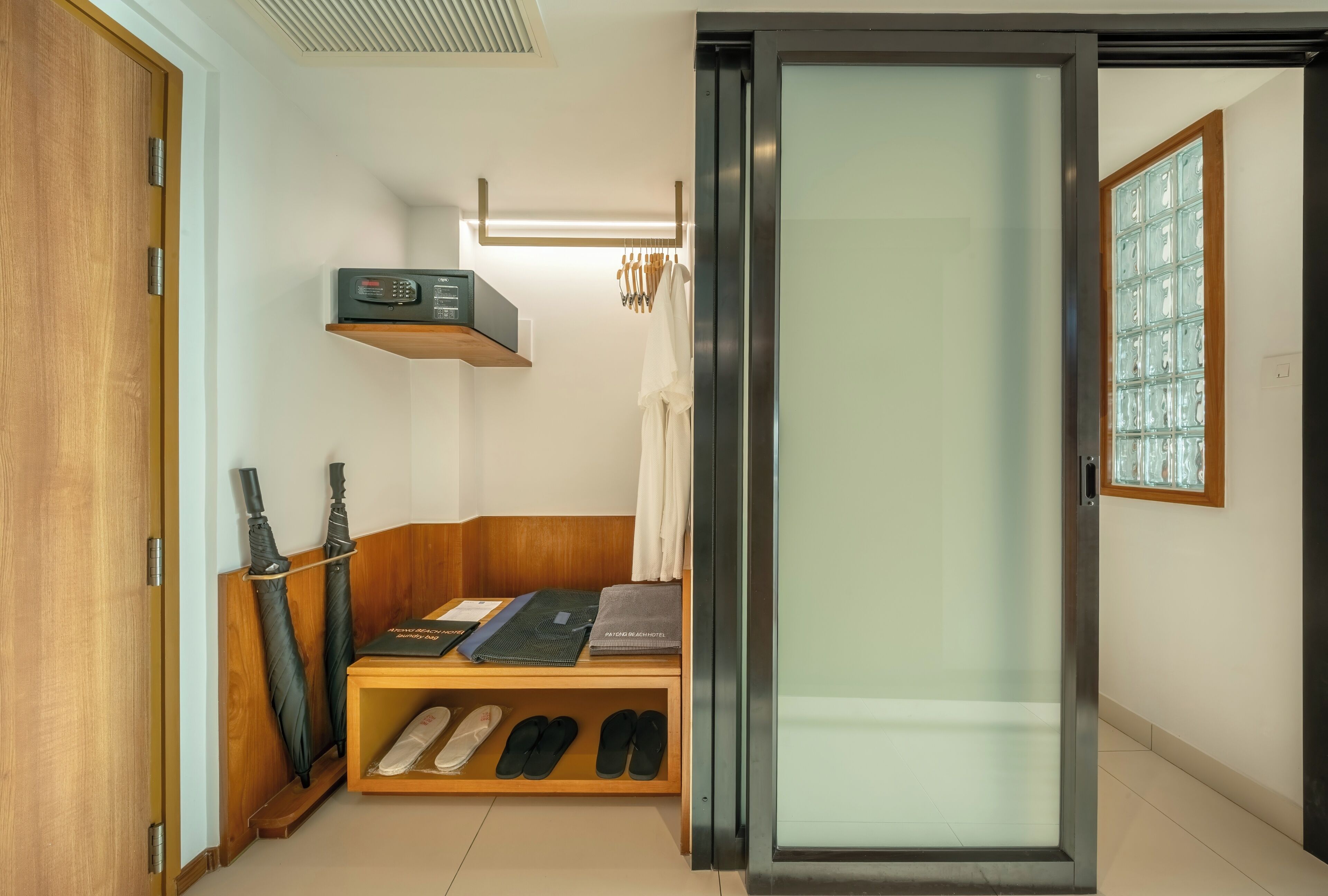 Ein Hotelzimmer mit einem Holzschrank, einem Regal mit einem Radio, einem Bett mit einer Decke, einem Paar Hausschuhen und einer Glastür.