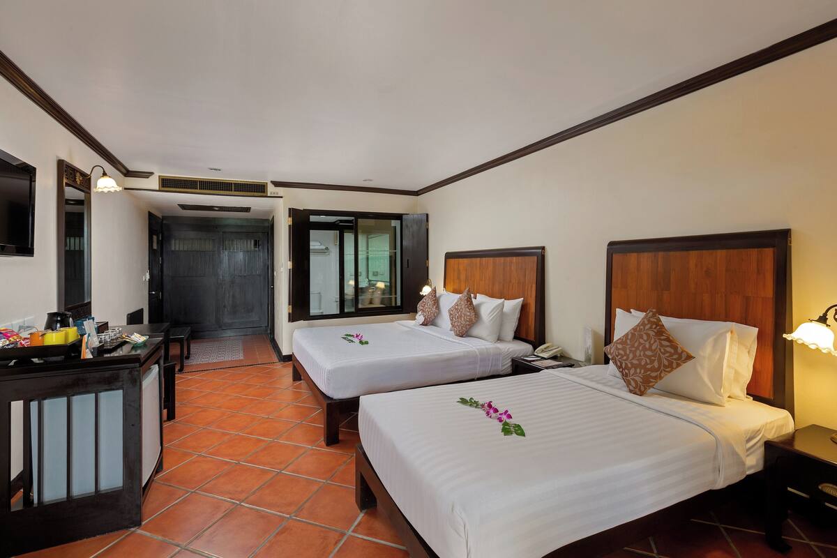 A hotel room with two beds, a desk, a chair, and a small kitchenette.