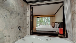 A bathroom with a large bathtub, marble walls, and a view of a bedroom through a mirror. - The Front Village (Karon)