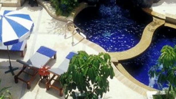 A resort pool area with a waterfall feature, lounge chairs, and umbrellas. - Karon Princess Hotel (Karon)